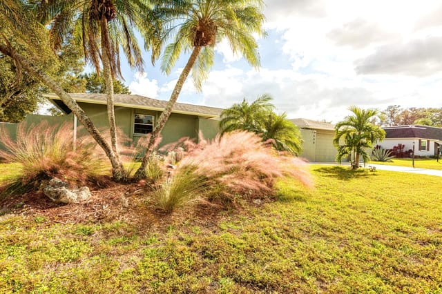 Front of the home with parking for 4 cars in driveway and tropical landscaping